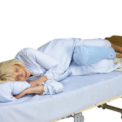 A person sleeps on their side with a SkiL-Care Ultra-Soft Bed Bolster placed between their knees on a blue-sheeted bed.