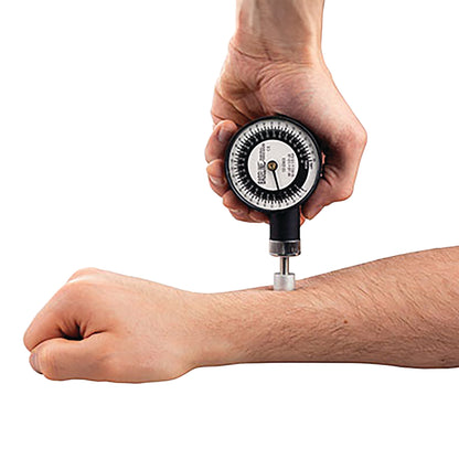 A hand uses the Baseline Mechanical Push/Pull Dynamometer to measure force on a forearm. The device has a round gauge display.