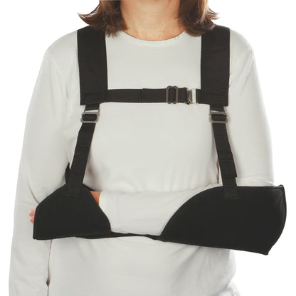 Woman wearing a Harris Hemi-Arm Sling, supporting the arm with black straps and a chest buckle, over a white shirt.