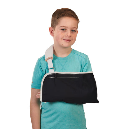 A young boy wears a Fits-All Sling, featuring a black arm support and white shoulder strap, over a turquoise shirt.
