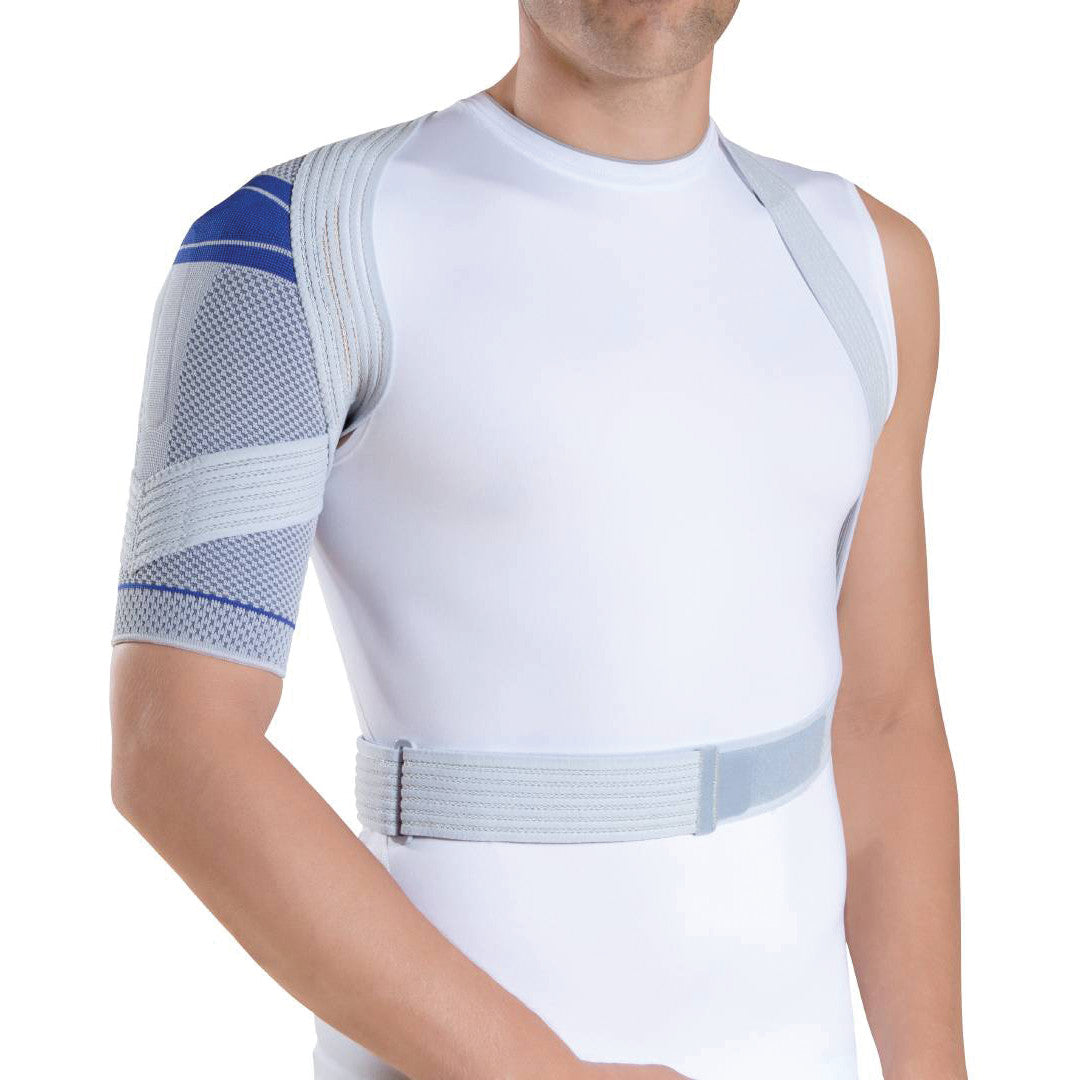 A person wears a Bauerfeind OmoTrain Active Shoulder Support over a white shirt, featuring a blue and gray mesh design.