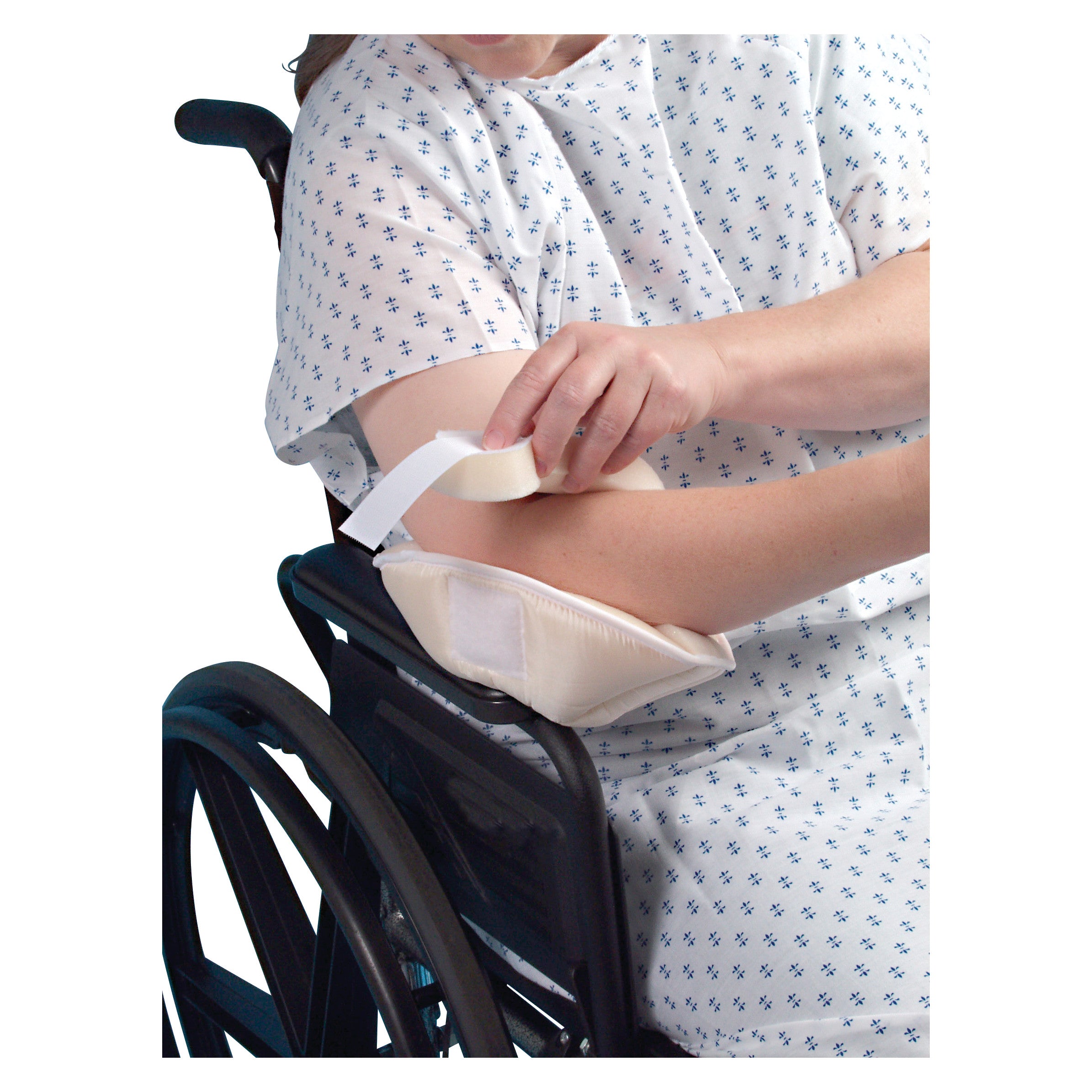 A person in a wheelchair adjusts an Elbowlift Suspension Pad on their elbow. They are wearing a patterned hospital gown.