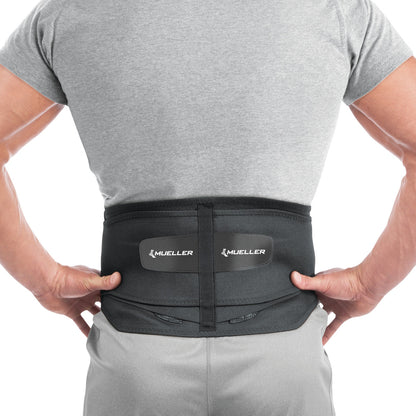 A person wears a Mueller Adjustable Back Brace over a gray shirt, showing its fit and support on the lower back.