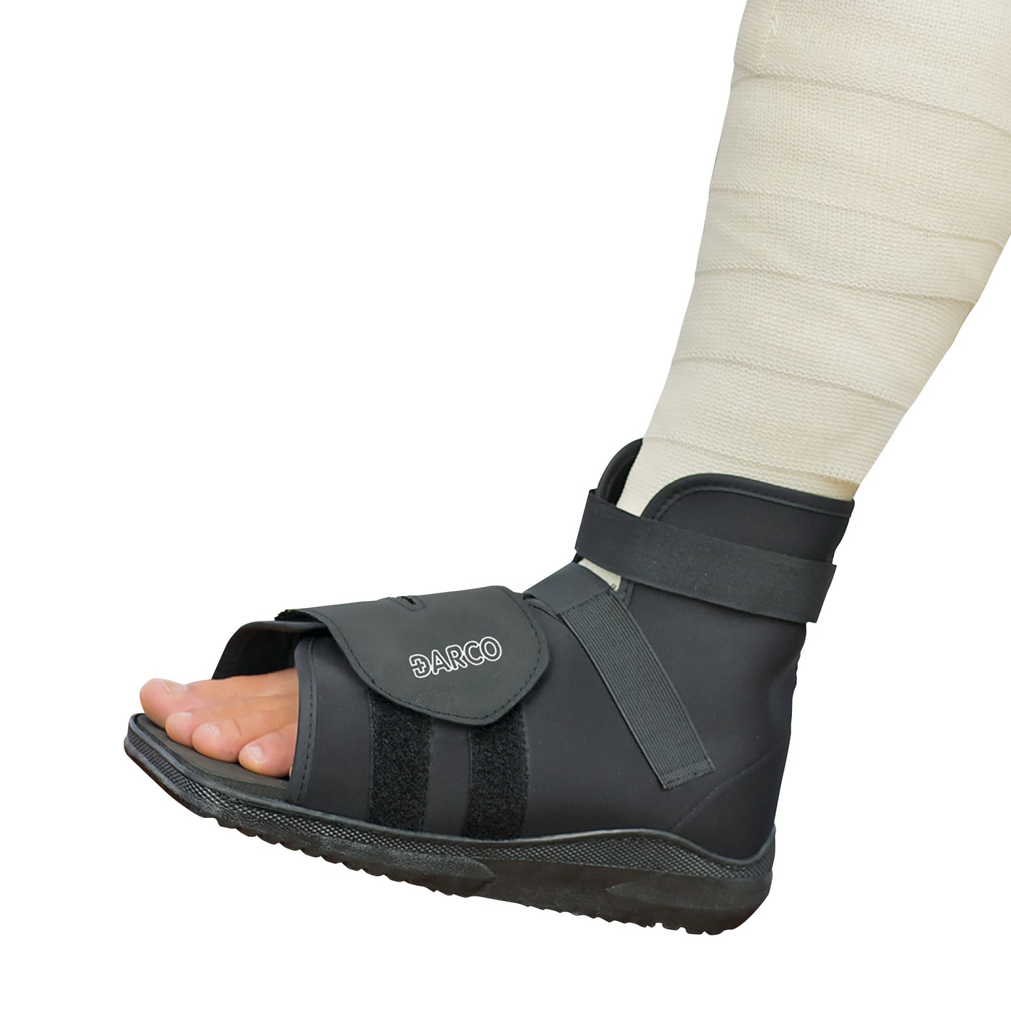 A close-up of a foot wearing a DARCO Slimline Cast Boot with an adjustable strap, over a wrapped leg.