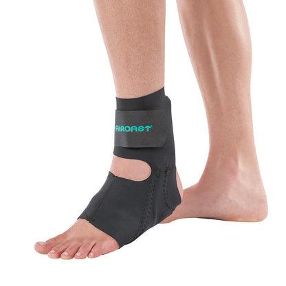 A person's left foot wearing an Aircast Airheel Brace, a black ankle support with an open heel design and strap closure.