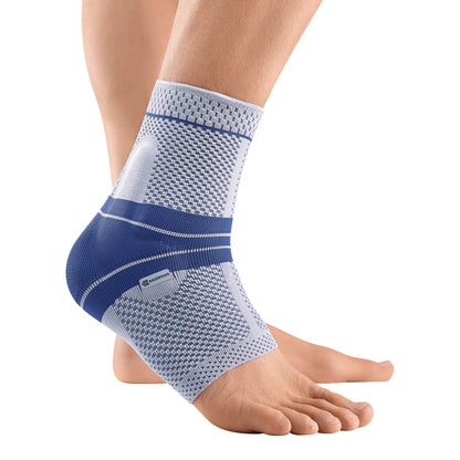 A foot wears a Bauerfeind MalleoTrain Ankle Support in blue and white, providing compression and stability to the ankle.
