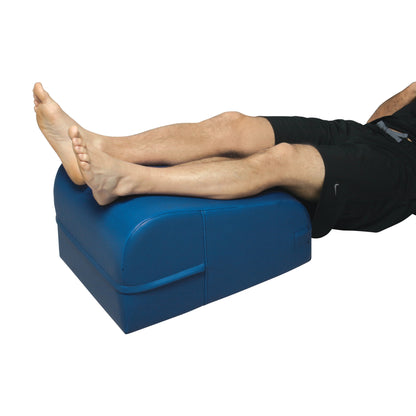 Person's legs rest on an AliMed Lower Extremity Wedge, a blue foam support cushion designed for leg elevation.