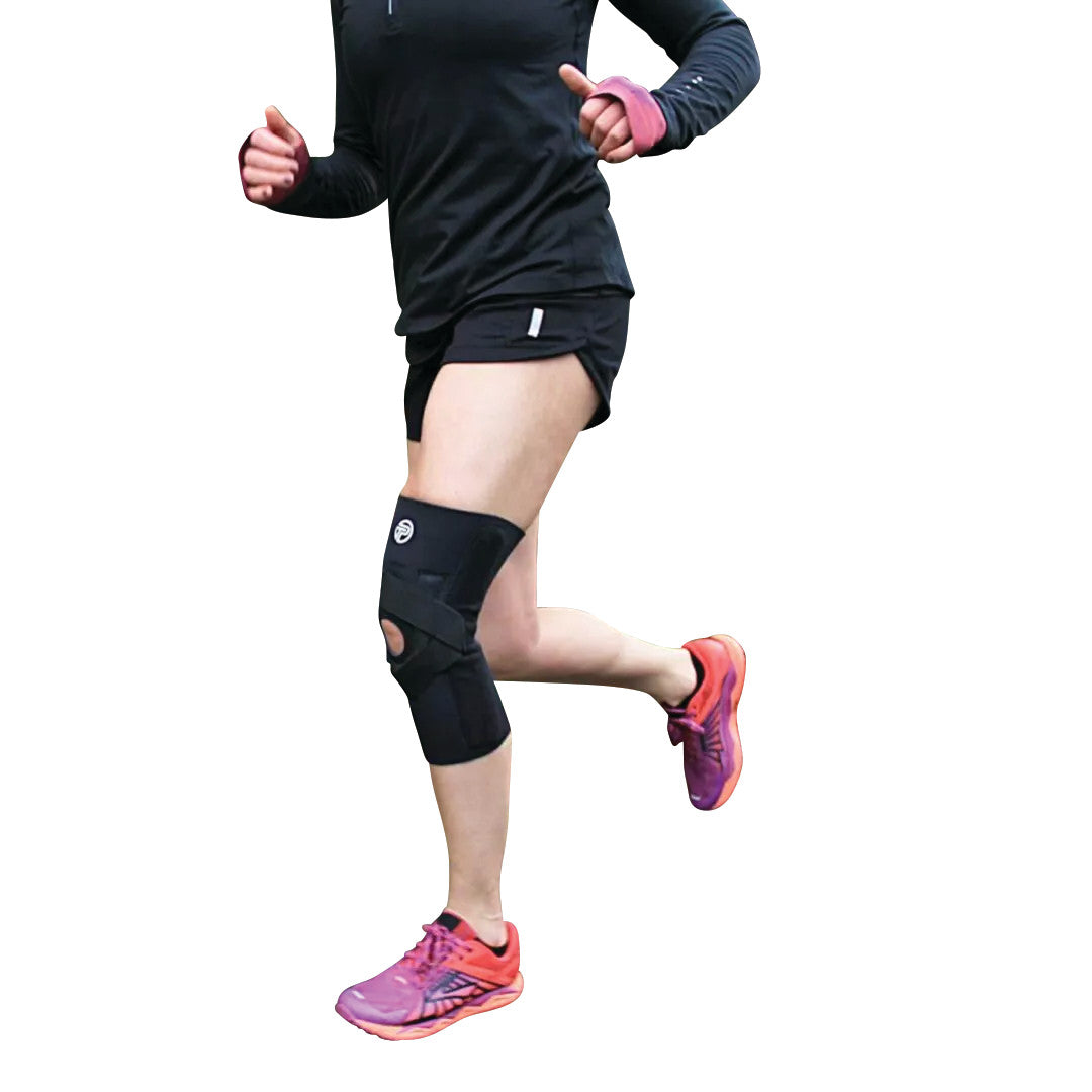 Person running, wearing a J-Lat Knee Support on the right knee, dressed in a black outfit and pink running shoes.