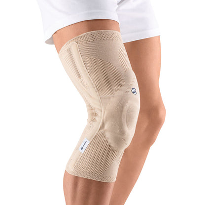 A person wears a Bauerfeind GenuTrain P3 knee brace, beige-colored, providing support just below the shorts.