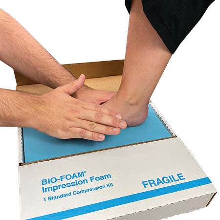 A person presses a foot into the BIO-FOAM Impression Foam Standard Kit, making an imprint on the foam in a cardboard box.