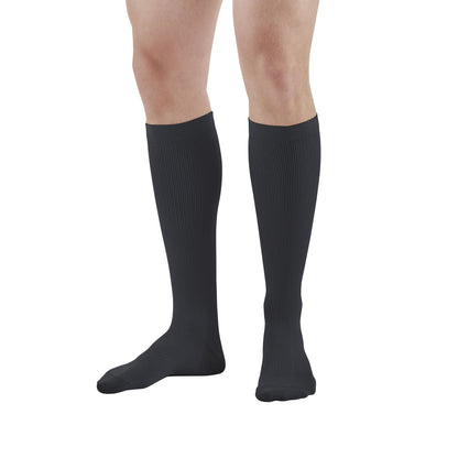 A person wears black Ames Walker Knee-Length Microfiber Support Socks, covering their lower legs to just below the knees.