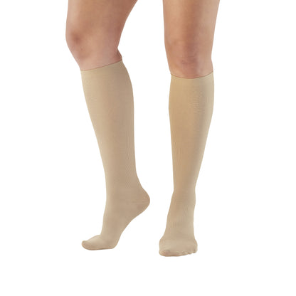 A person wears Ames Walker Knee-Length Microfiber Support Socks in beige, standing on a white background.