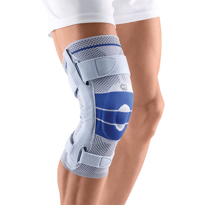 The Bauerfeind GenuTrain S Knee Brace is worn on a leg. It features blue and gray fabric with adjustable straps for support.