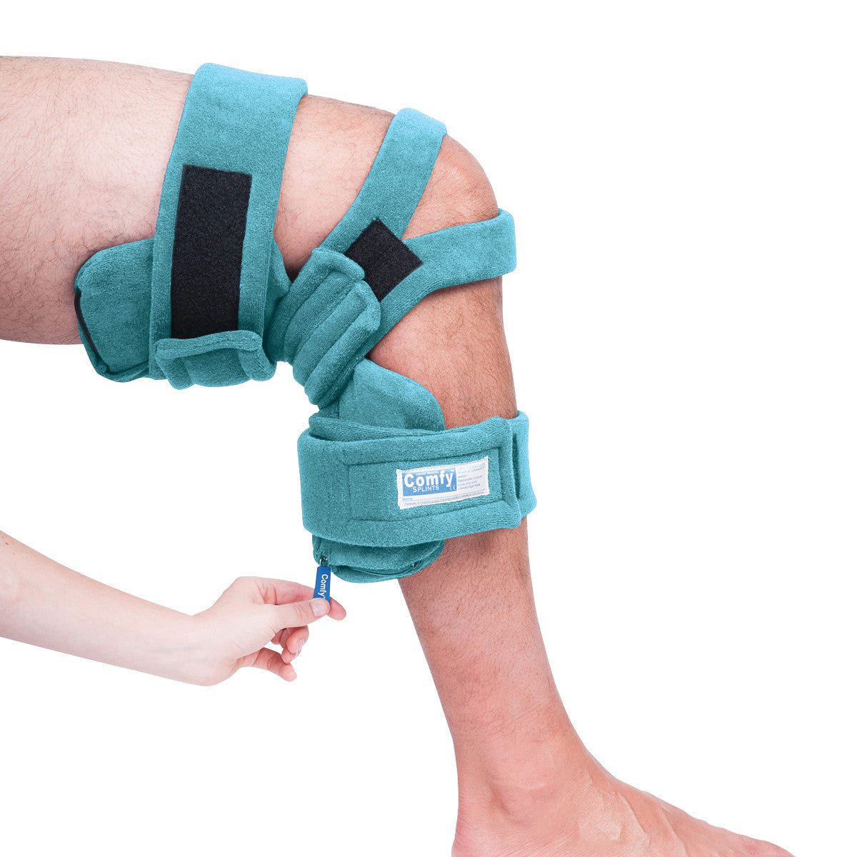 A person's bent knee is fitted with a teal Comfy Splints Pediatric Locking Knee Orthosis. A hand adjusts a strap on the device.