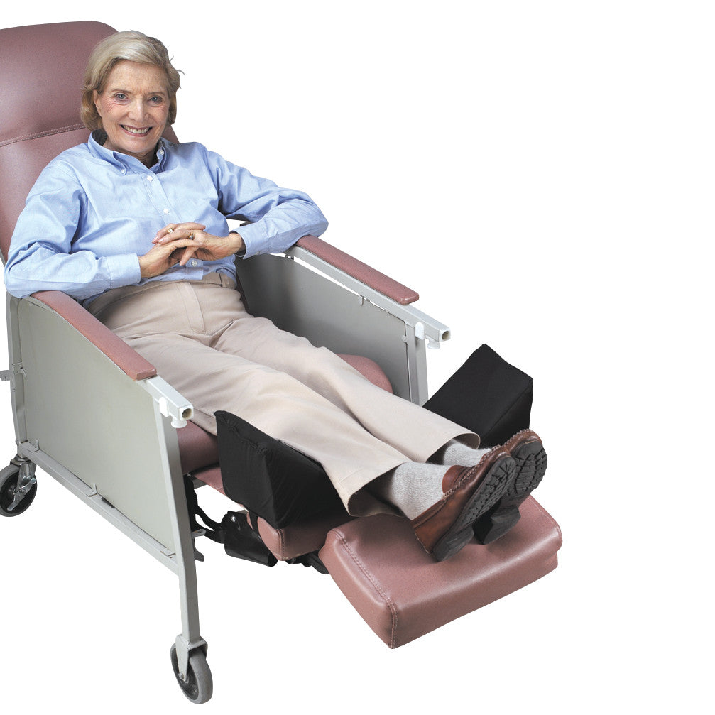 A person sits comfortably in a reclined chair using the SkiL-Care Geri-Chair Leg Positioner to elevate and support their legs.