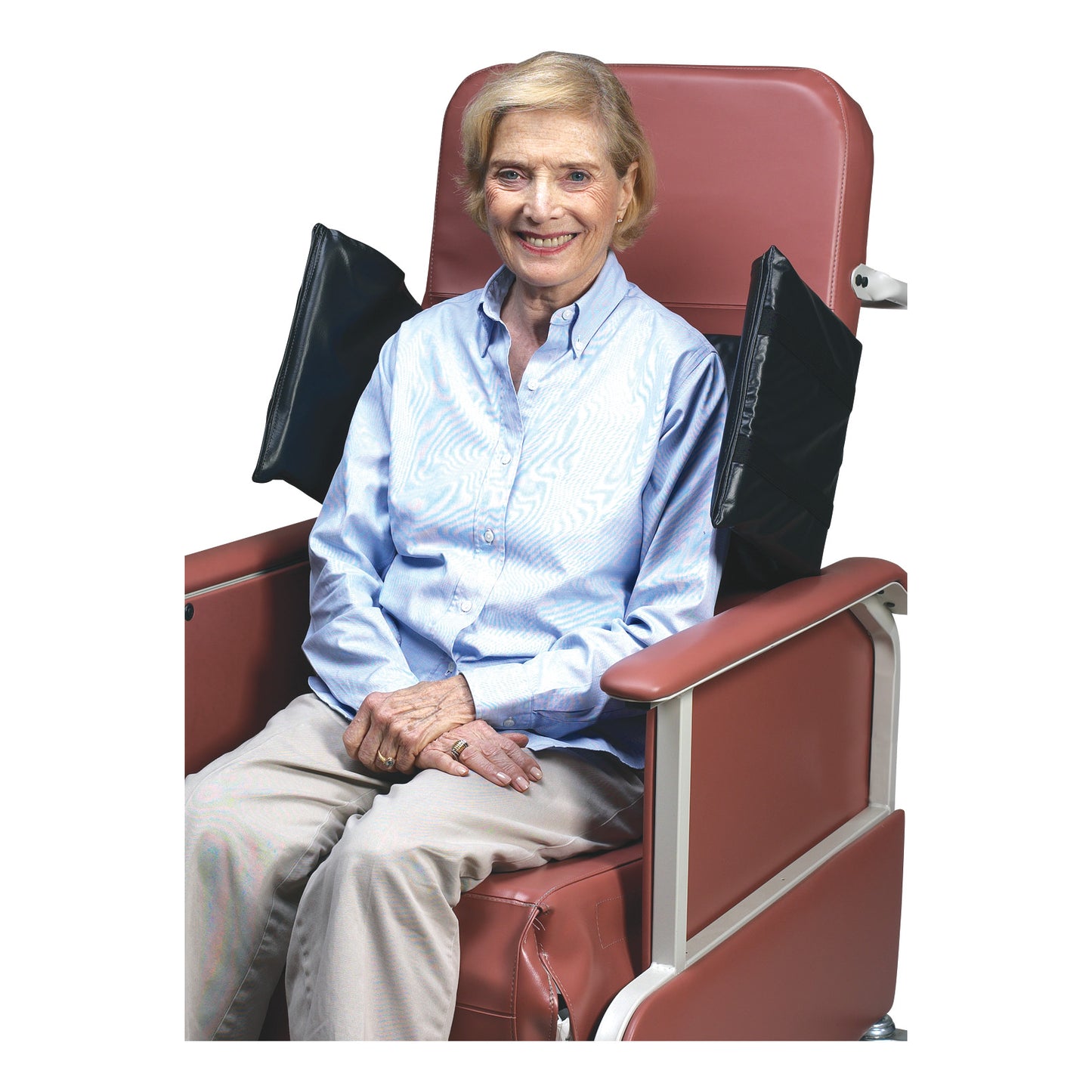 An elderly woman sits in a chair equipped with SkiL-Care Geri-Chair Side Wings. The wings are attached to the chair's upper sides.