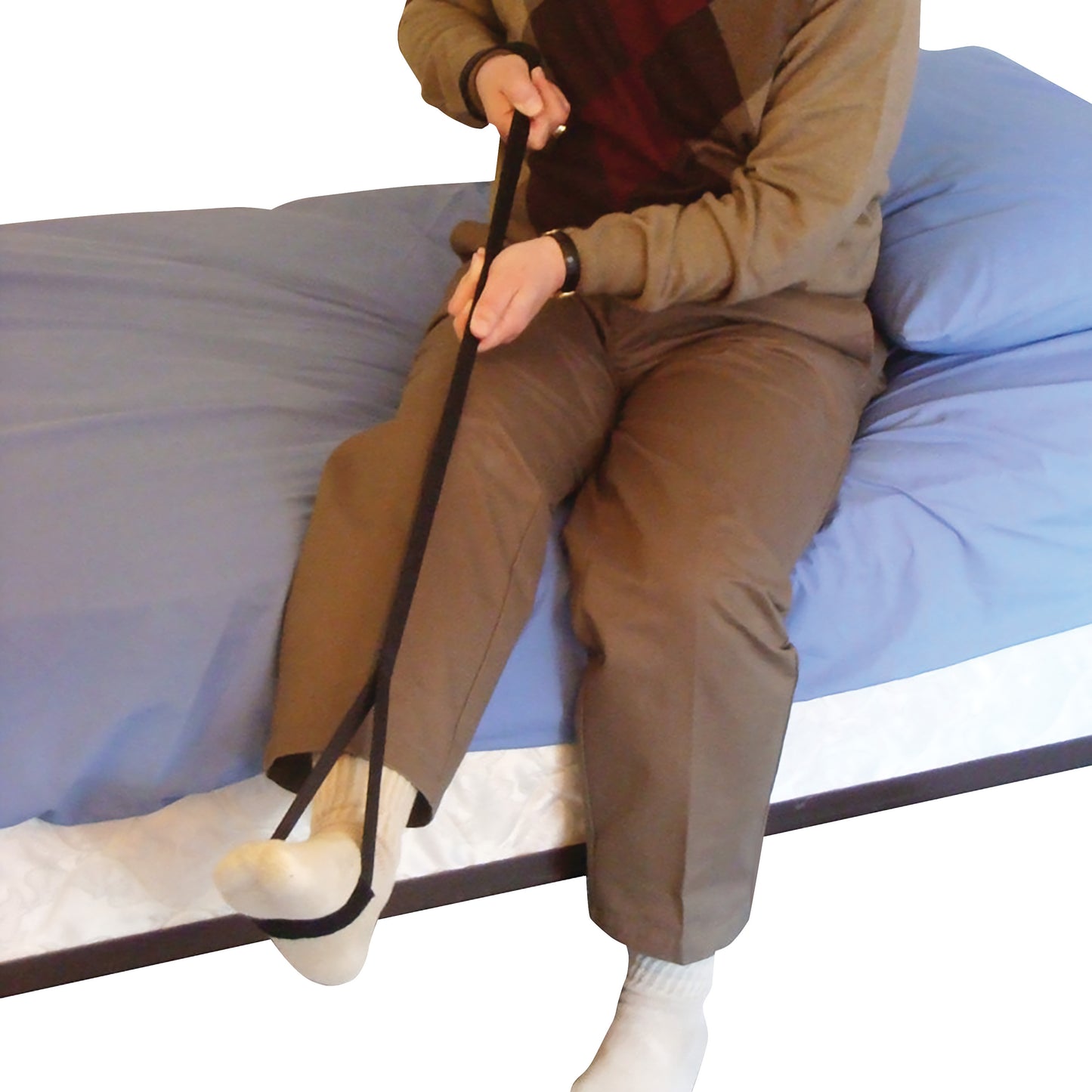 A person uses the SafetySure Leg Up, a strap aiding in lifting the leg, while seated on a bed with blue sheets.