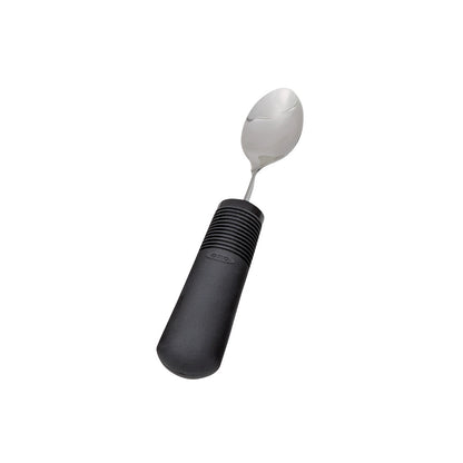 A spoon from the Good Grips Standard Utensils line, featuring a wide black handle with textured grip and a metal spoon head.