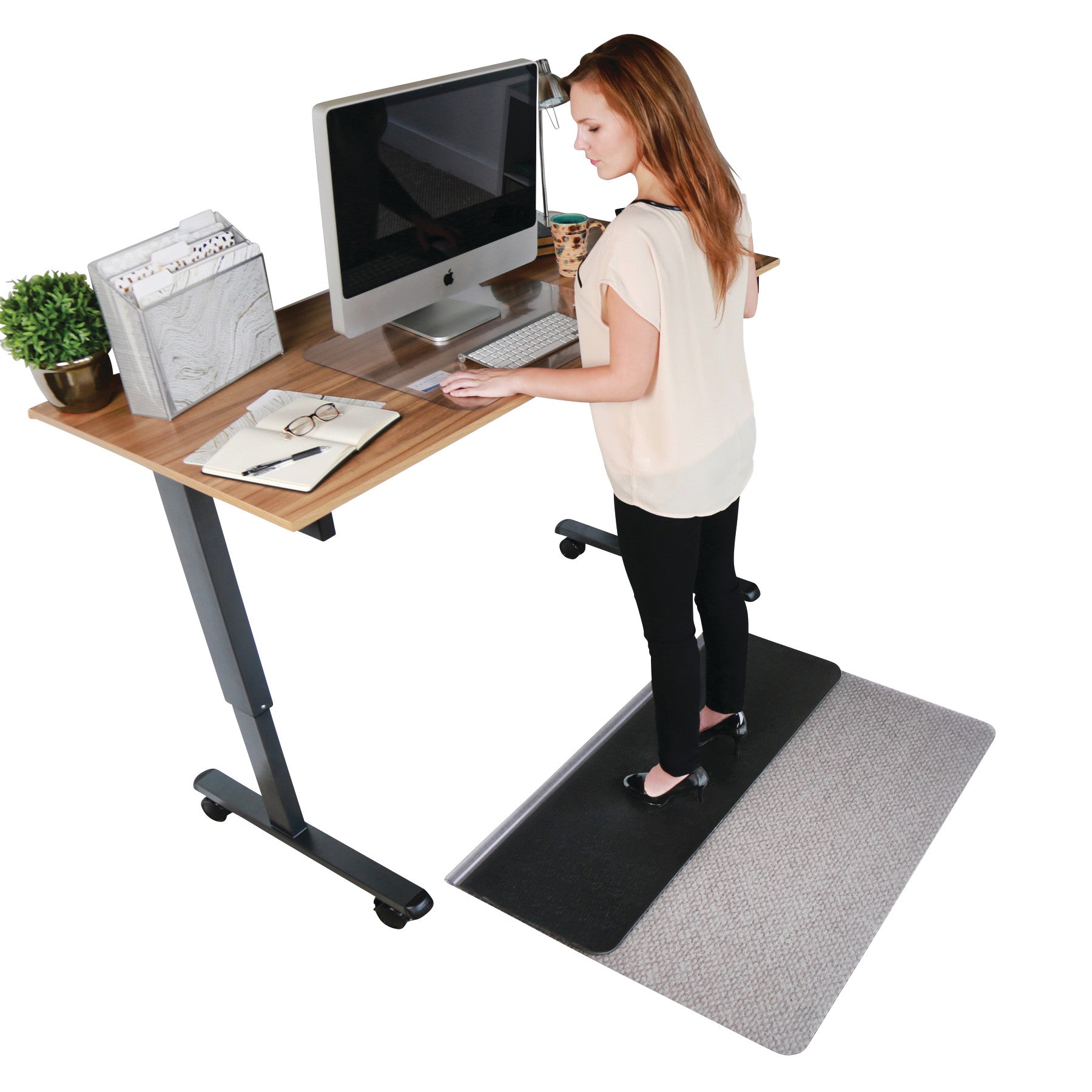 A woman uses a computer at a standing desk on an Aleco Sit or Stand Mat, which is layered over a carpeted floor.
