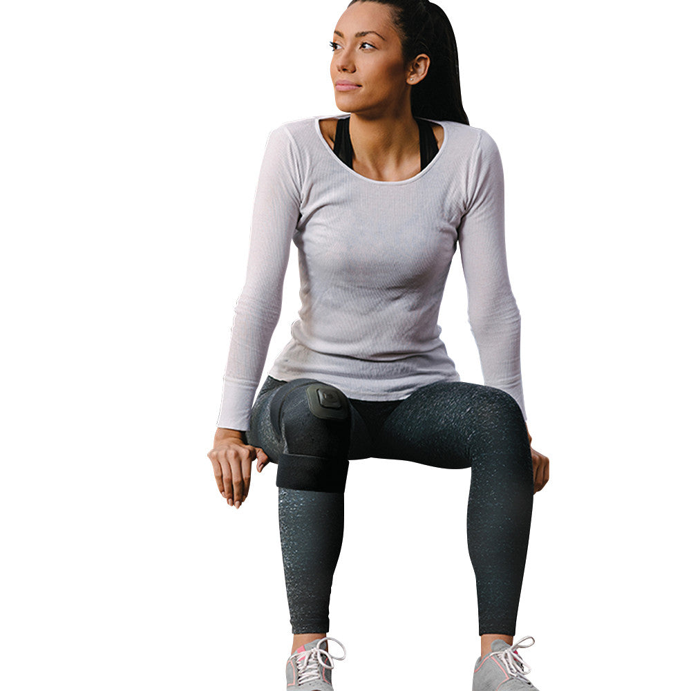 A woman wearing the Intellinetix Knee/Elbow Therapy Wrap on her knee, sitting in activewear against a plain background.