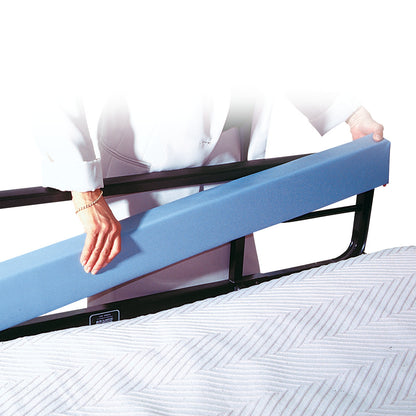 A person places the AliMed Bed Stuffer Safety Bolster, a blue foam cushion, between a bed rail and mattress for added protection.