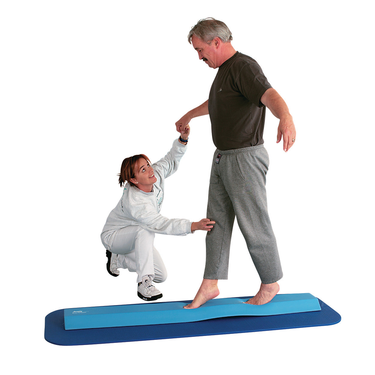 A man balances on an AIREX Balance Beam, assisted by a woman. They are on a blue mat, focusing on stability exercises.