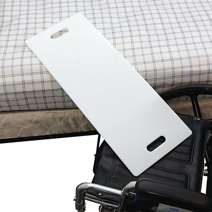 A SafetySure Transfer Board bridging a wheelchair and a bed with a checkered sheet. The board has handgrips for easy handling.