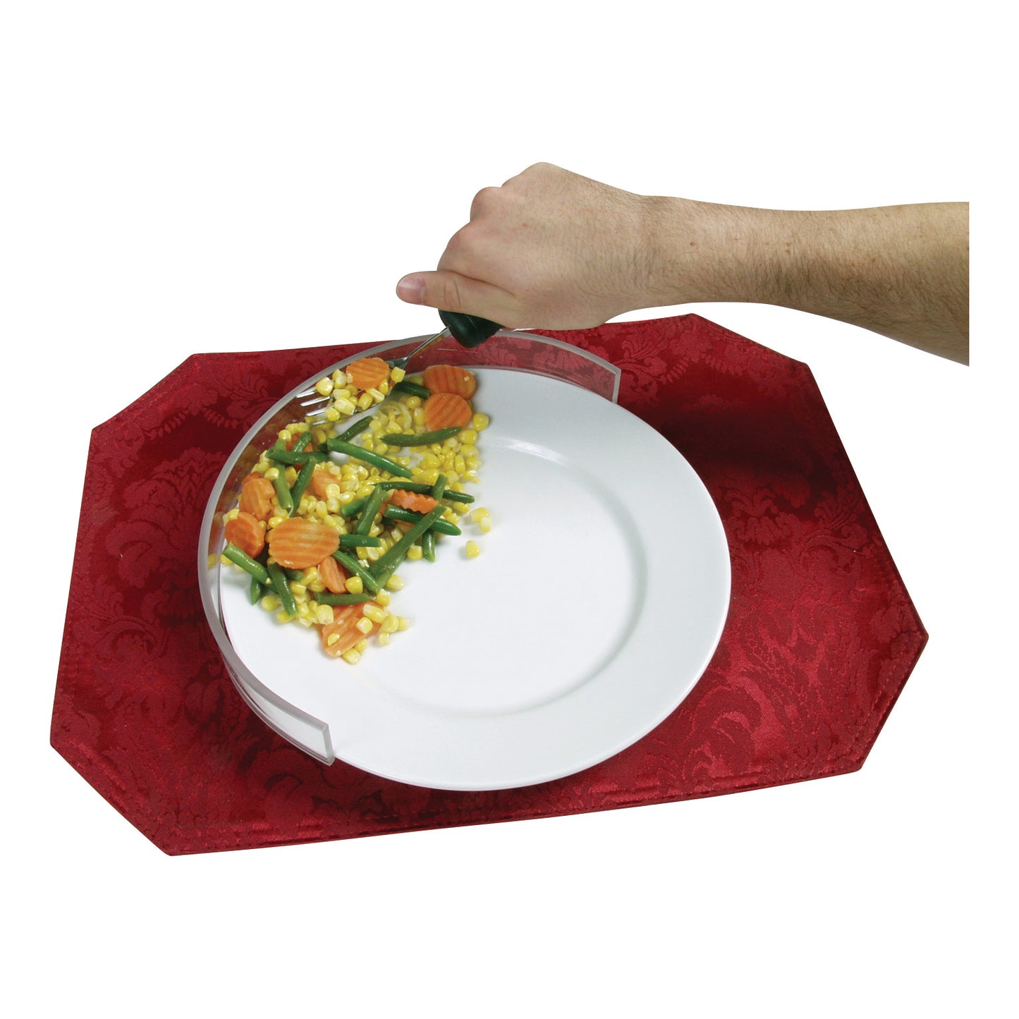 A hand uses the Therafin Plate Guard to scoop mixed vegetables onto a white plate on a red placemat.