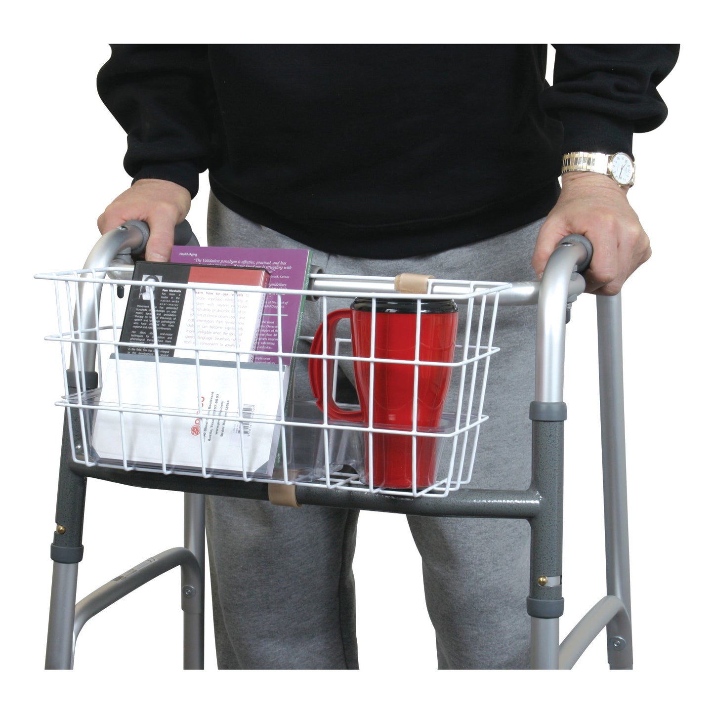 A person uses an AliMed Walker Basket attached to a walker, holding items like a red mug and a book.