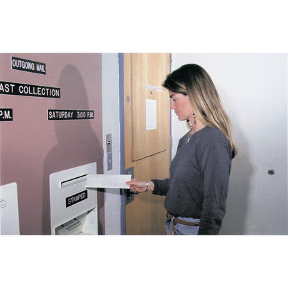 A person is using Advanced Descripto-Cards to mail something. They are placing it in an "Outgoing Mail" slot on a wall.