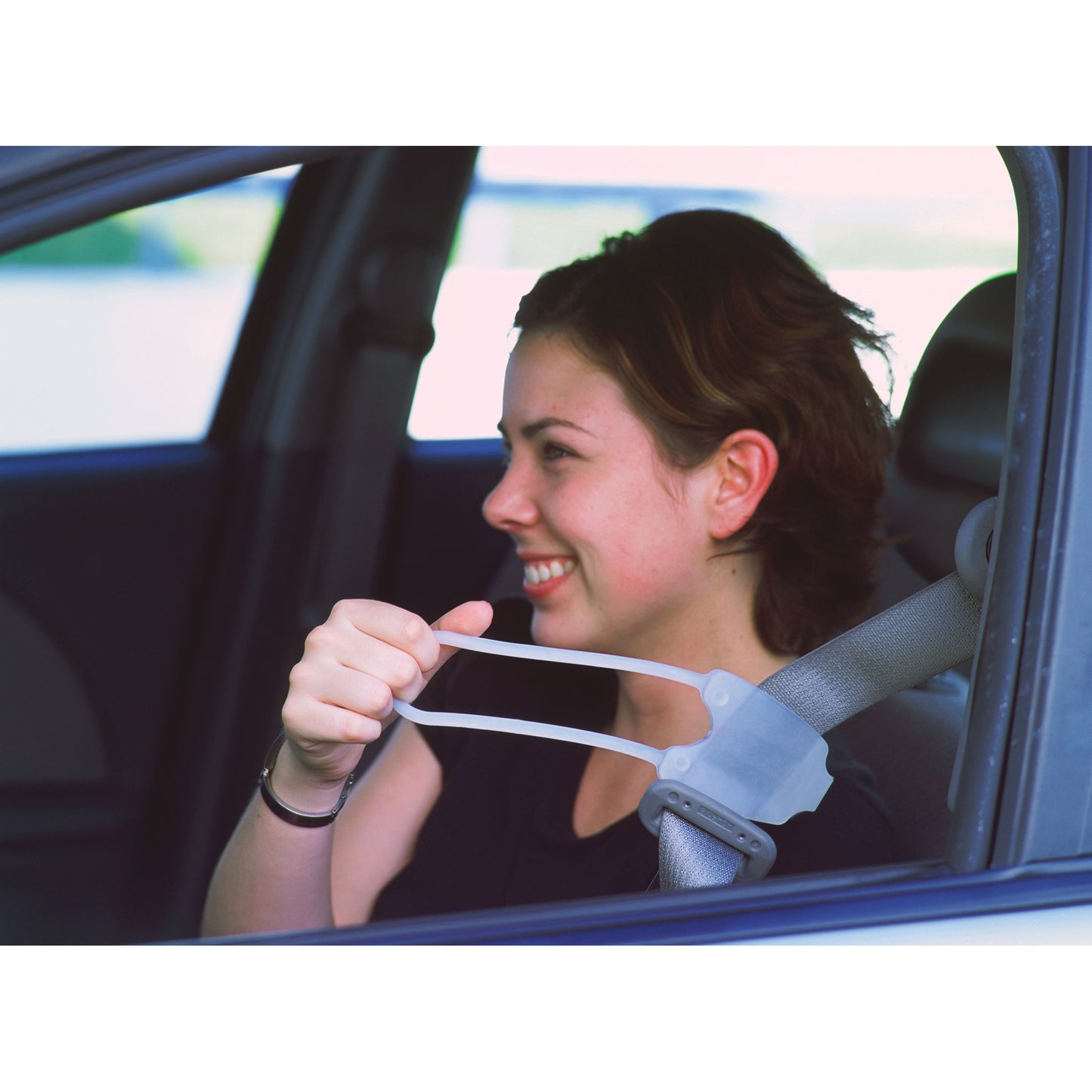 A person in a car uses the Easy Reach Seat Belt Handle to buckle the seatbelt, smiling while pulling it forward for easier reach.