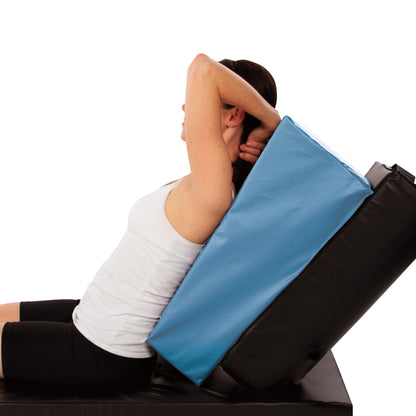 A person leans back using the AliMed AP Upright Positioner, with arms raised, wearing a white tank top and black shorts.