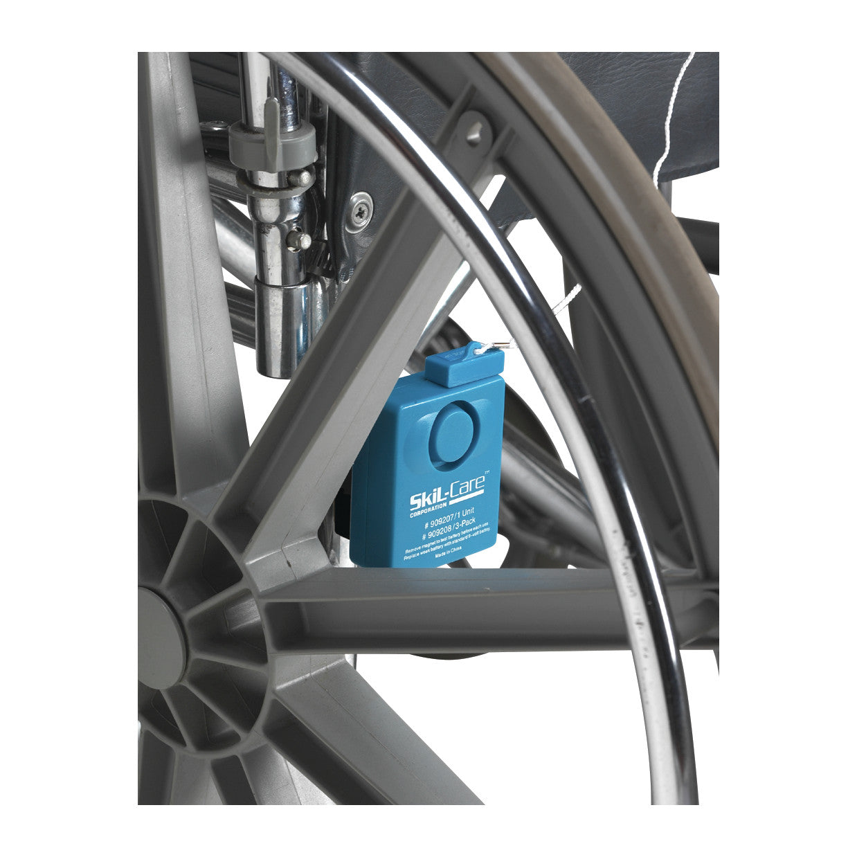 Close-up of a grey wheelchair wheel with a blue device labeled "SkiL-Care Wheelchair Econo Alarm" attached to it.