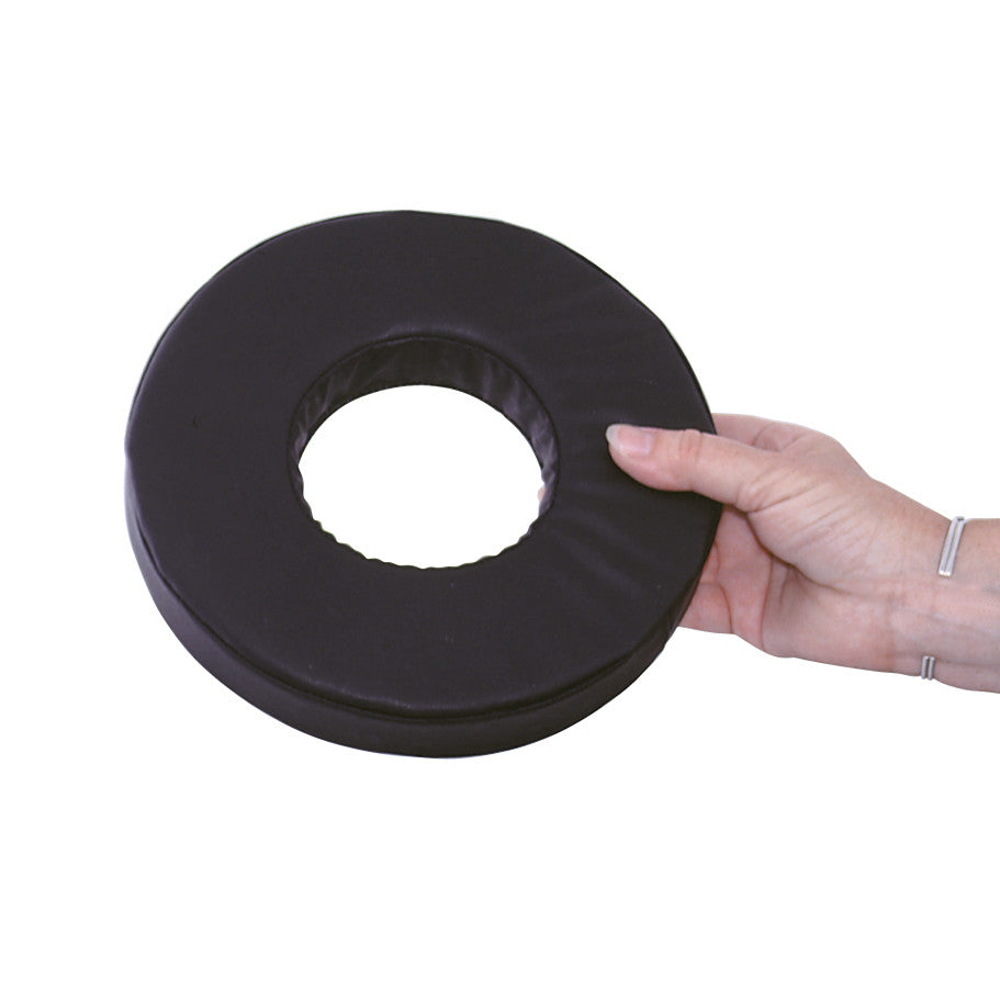 A hand holds the AliMed Conductive Black Vinyl-Covered Head Donut, which is a round, padded support with a central hole.