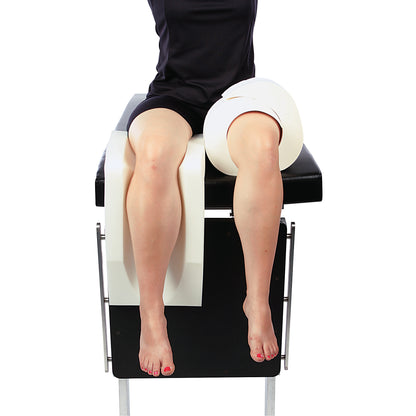 A person sits on a medical table with an Arthroscopic Well Leg Holder and Knee Kit supporting one leg.
