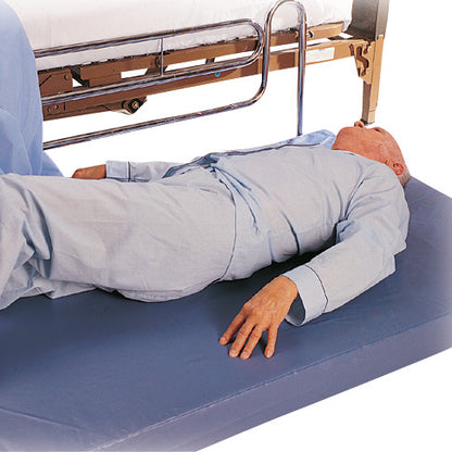 A person lies on a SkiL-Care EasyClean Mat next to a hospital bed, wearing light blue pajamas.