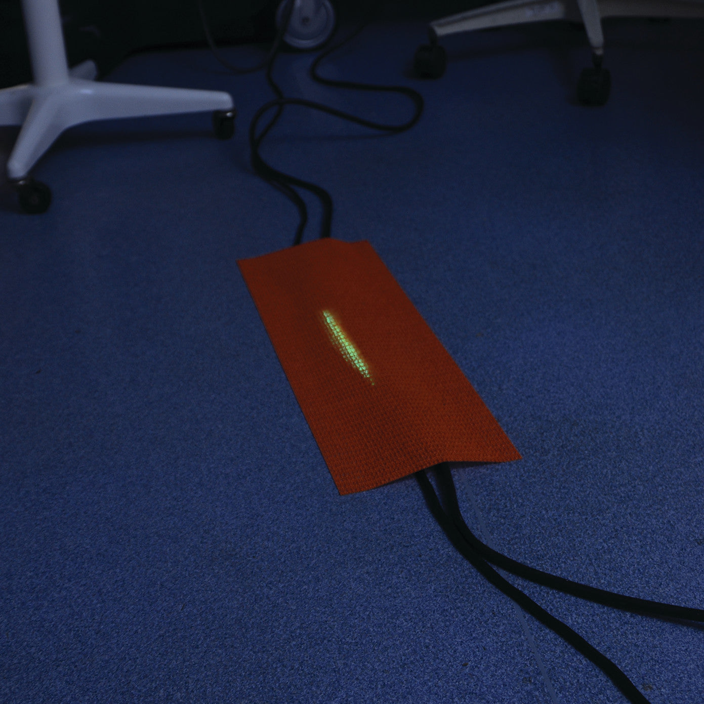 SANDEL Trip-No-More Cord Alert covers floor cables with an orange, textured strip, highlighted with a glowing green line.