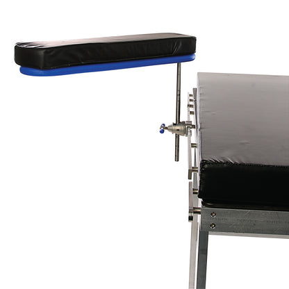 The AliMed Radiolucent Armboard with Pad is attached to a medical table, featuring a black cushioned arm support and metal frame.