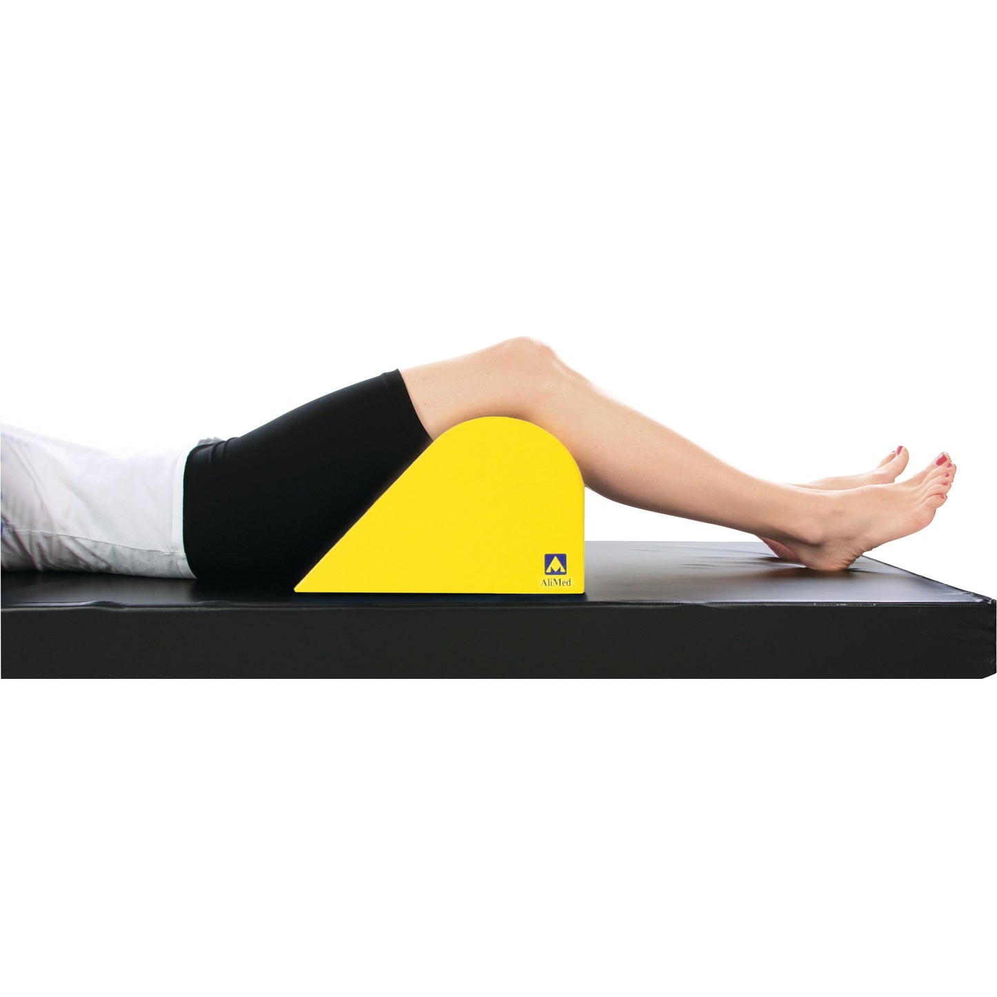 A person lies on a black mat using an AliMed Protecta-Coat Standard Knee Bolster. The yellow bolster supports the knees.