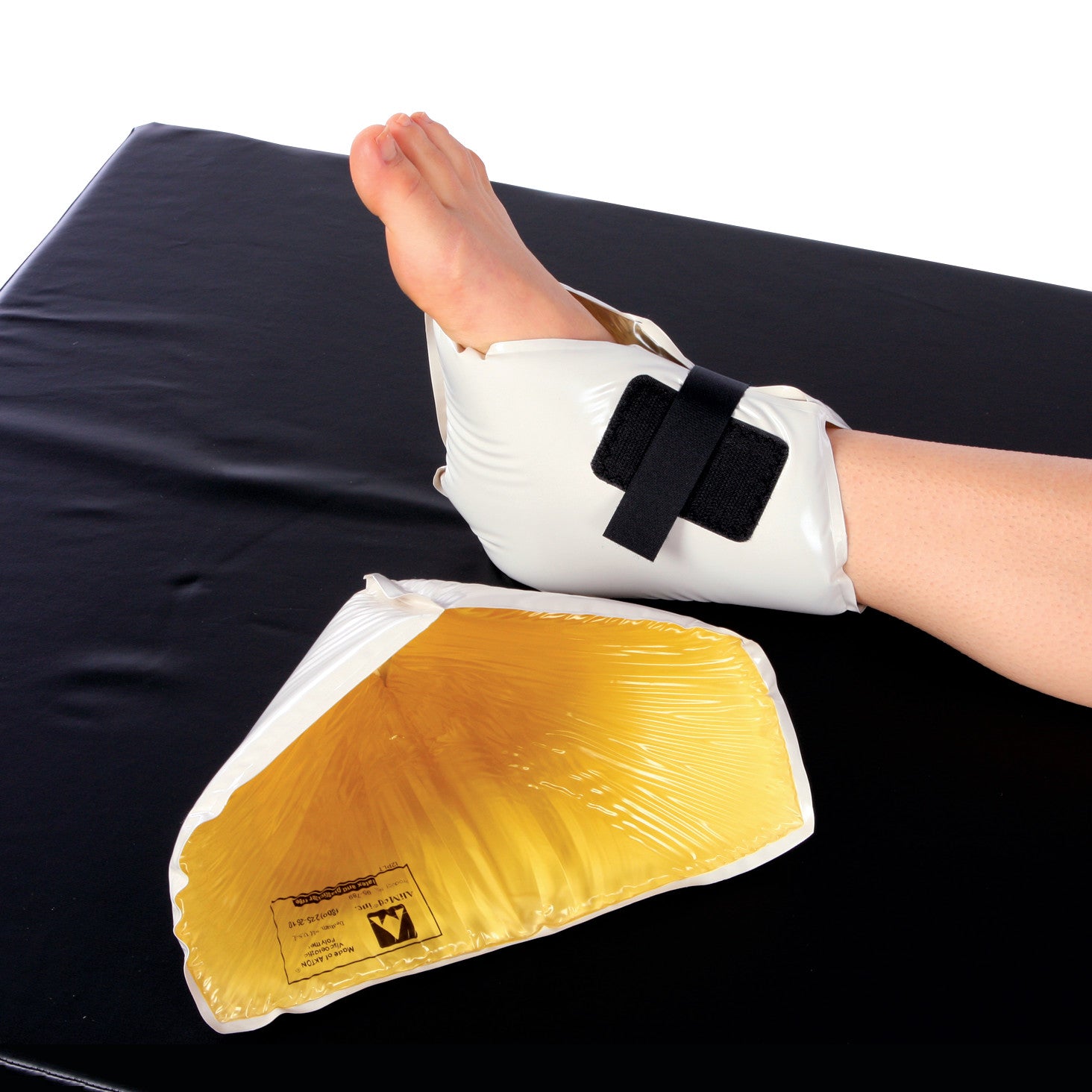 A foot wearing the AliMed AliGel Heel Protector Wrap, featuring a white exterior and black strap, next to an open yellow gel wrap.