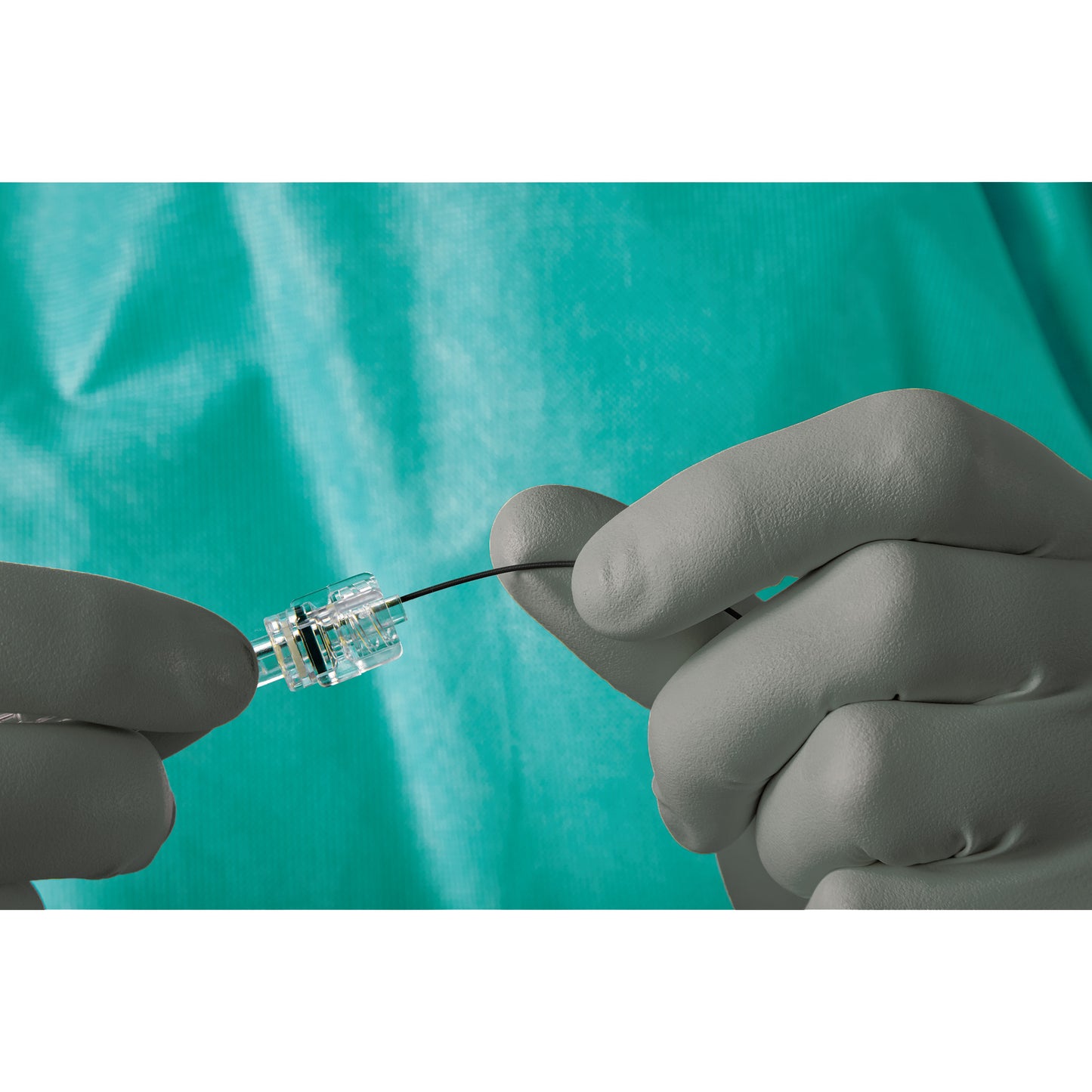 A person wearing AliMed AliGuard Radiation Attenuation Gloves holds a medical device with a clear connector and a thin black wire.