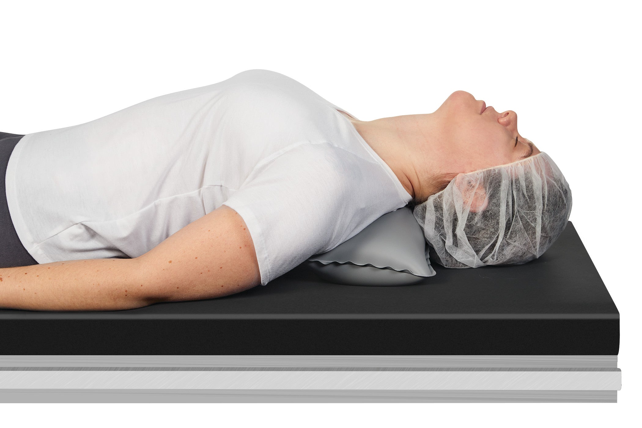 A person is lying on a table using the AliMed Adjustable Surgical Thyroid Positioner for neck support, wearing a hair cover.