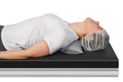 A person is lying on a table using the AliMed Adjustable Surgical Thyroid Positioner for neck support, wearing a hair cover.