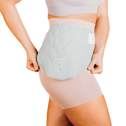 Woman wearing the Xena Therapies Opal Cool One wrap on her lower back, over light pink shorts and a matching top.
