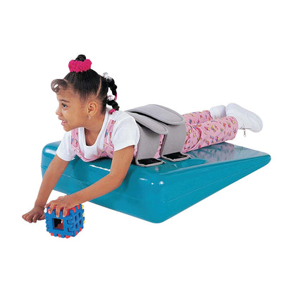 A child is lying on the Tumble Forms2 20 Degree Deluxe Strap Wedge, holding a colorful toy block, with straps securing the child.