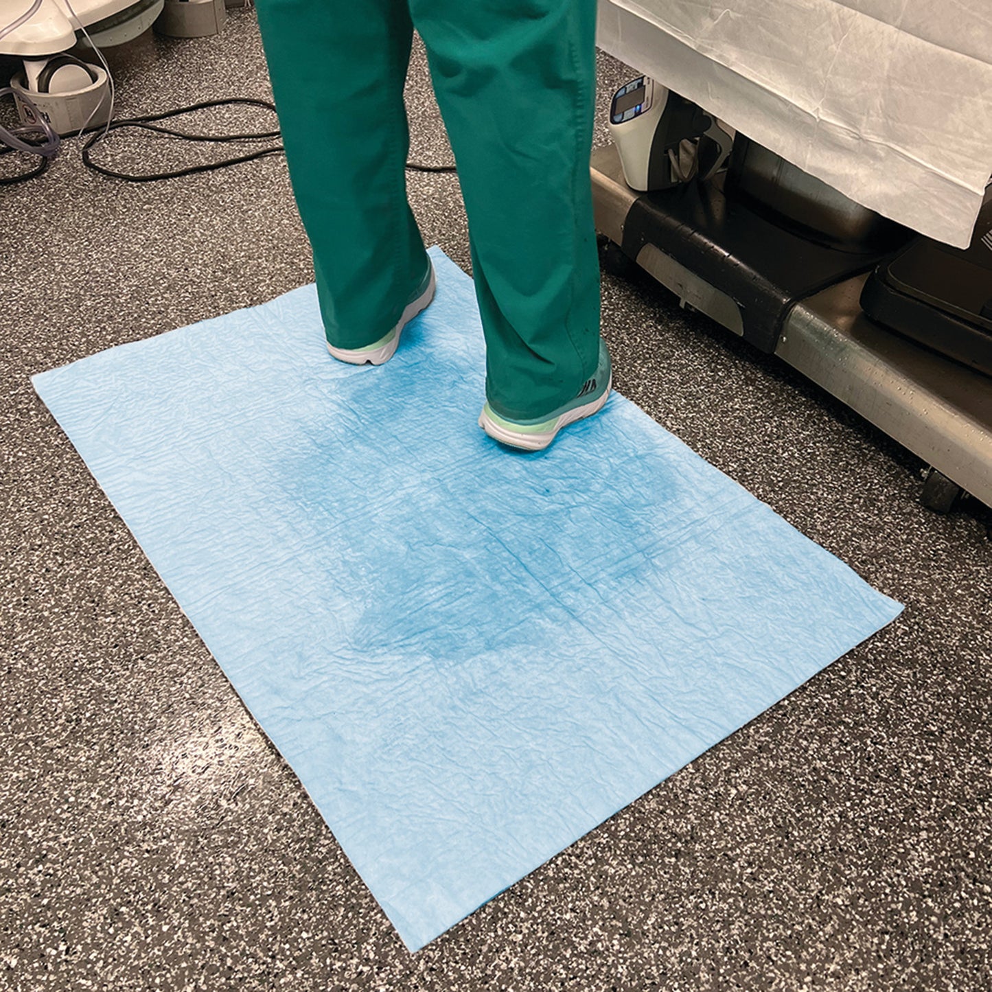 Person standing on a SpilfyterMED Blue Absorbent Mat for Heavy Spillage in a medical setting, covering a textured floor.