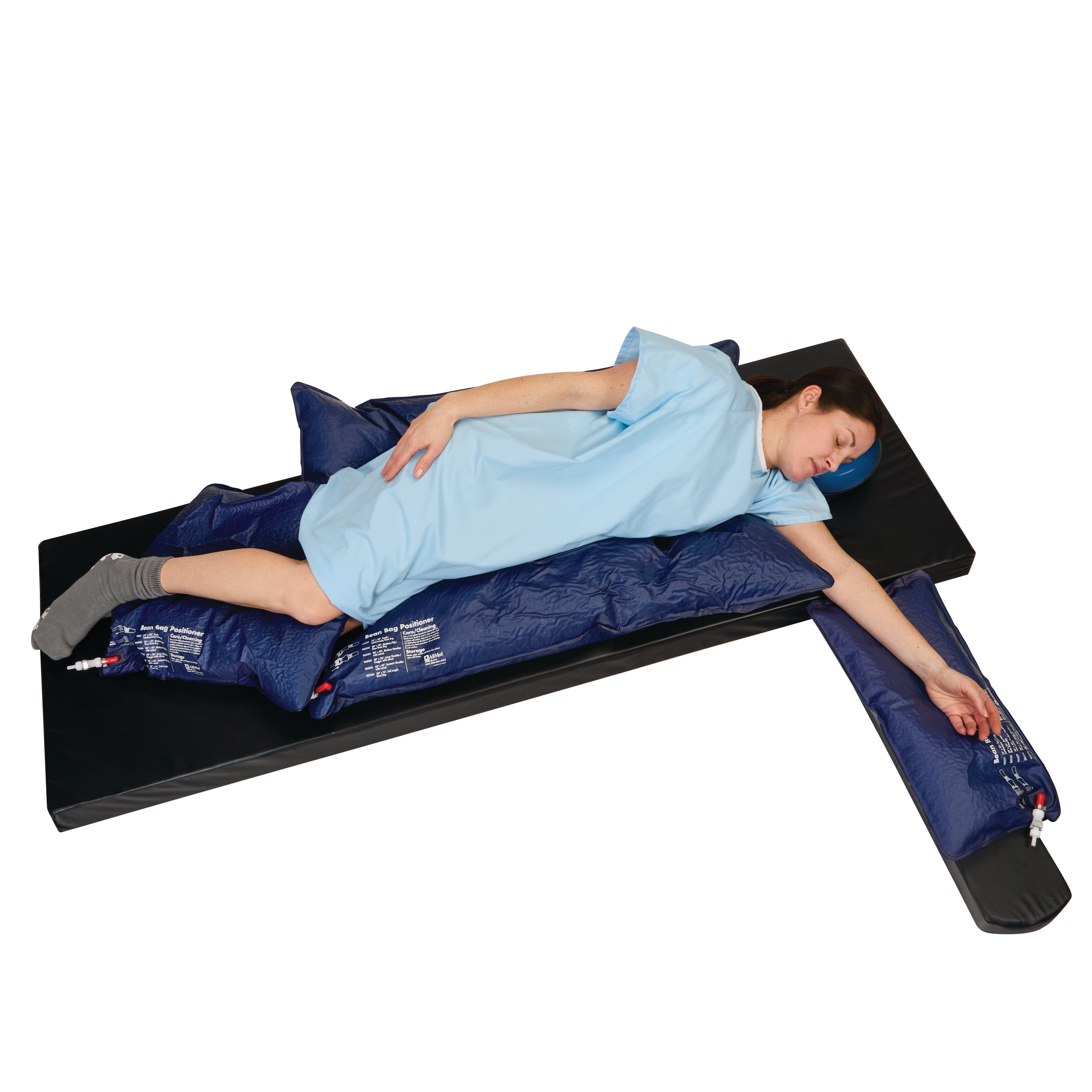 A person lies on a black mattress using the AliMed Bean Bag Positioner with Cutout. They wear a blue gown and gray socks.