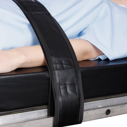 A person wearing a light blue gown is secured with an AliMed Nonmetallic Operating Room Table Strap, fastened over their arm.