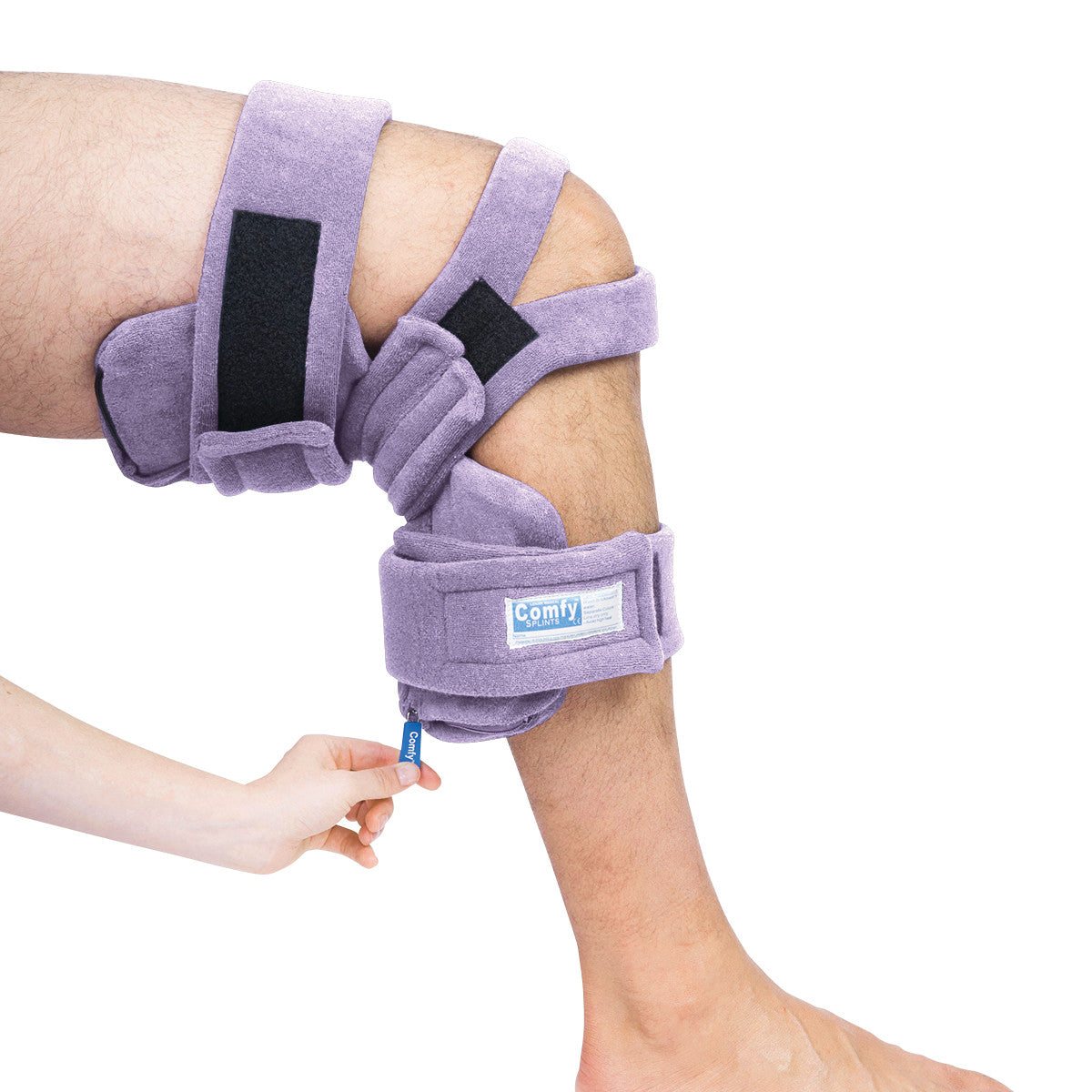 A purple Comfy Splints Pediatric Locking Knee Orthosis is worn on a bent knee. A hand adjusts the brace's strap.