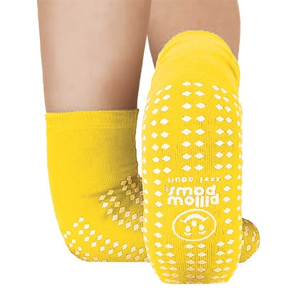 Two legs wearing yellow Pillow Paws Double Print Risk-Alert Socks with non-slip white patterns on the soles and sides.